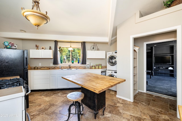 kitchen with stacked washer and dryer, wood counters, hanging light fixtures, black refrigerator, and white cabinets