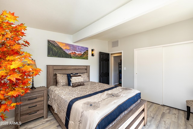 bedroom featuring a closet, beamed ceiling, and light wood-type flooring