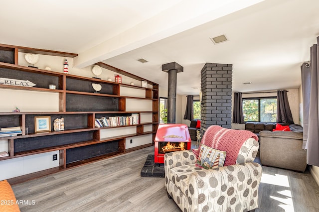 living area featuring a wood stove, vaulted ceiling with beams, and light wood-type flooring