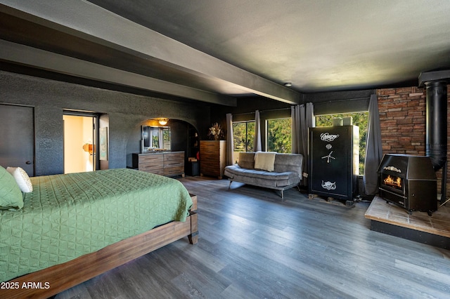 bedroom with hardwood / wood-style flooring, beamed ceiling, and a wood stove