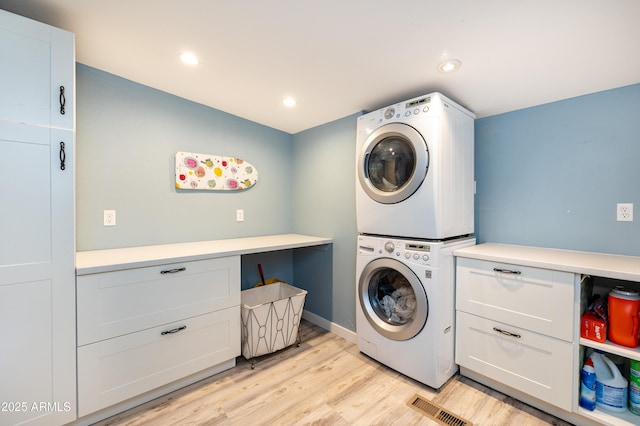 laundry room with cabinets, stacked washer / drying machine, and light hardwood / wood-style flooring