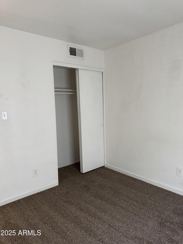 unfurnished bedroom featuring baseboards, visible vents, dark colored carpet, and a closet