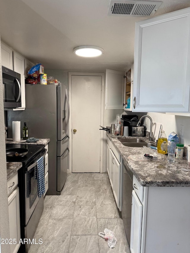 kitchen with visible vents, dark stone countertops, stainless steel appliances, white cabinetry, and a sink