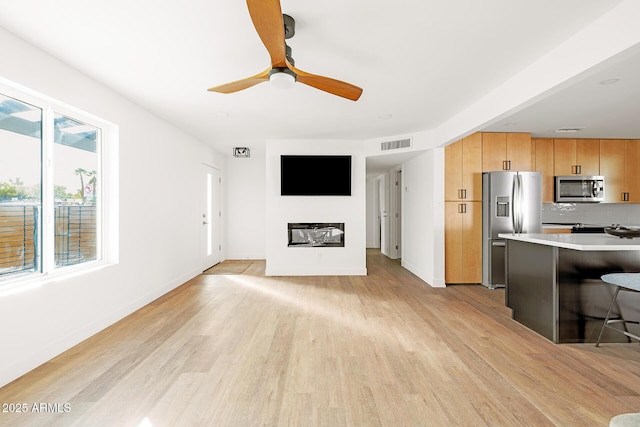 unfurnished living room featuring a wealth of natural light, light hardwood / wood-style floors, and ceiling fan