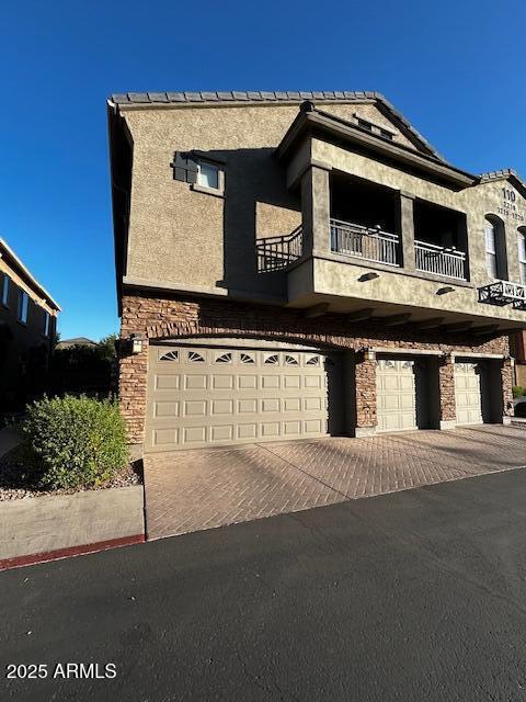 1350 S Greenfield Rd Unit 1219, Mesa, AZ 85206 - view of front facade featuring a balcony, a garage, driveway, and stone siding