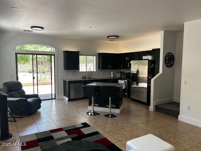 1350 S Greenfield Rd Unit 1219, Mesa, AZ 85206 - kitchen with stainless steel appliances, dark cabinets, a kitchen island, a kitchen bar, and light tile patterned flooring
