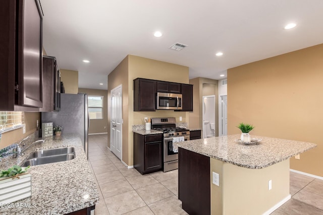 kitchen featuring light tile patterned floors, appliances with stainless steel finishes, a kitchen island, light stone counters, and sink