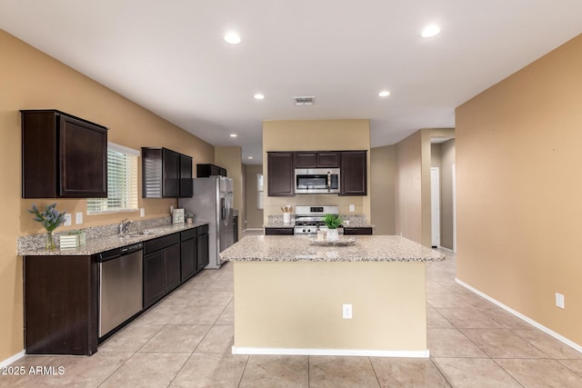 kitchen featuring light tile patterned floors, light stone counters, stainless steel appliances, and a kitchen island