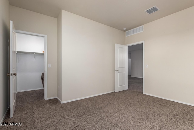 unfurnished bedroom with a walk in closet, a closet, and dark carpet