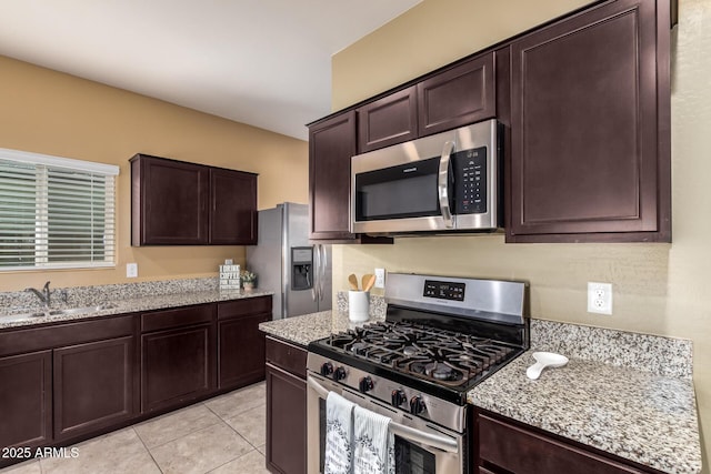 kitchen featuring light stone countertops, dark brown cabinetry, stainless steel appliances, sink, and light tile patterned floors