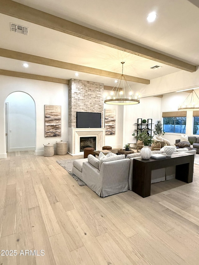 living room featuring beam ceiling, a large fireplace, a notable chandelier, and light hardwood / wood-style flooring