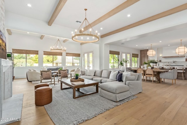 living room featuring plenty of natural light, a notable chandelier, beamed ceiling, and light wood-type flooring