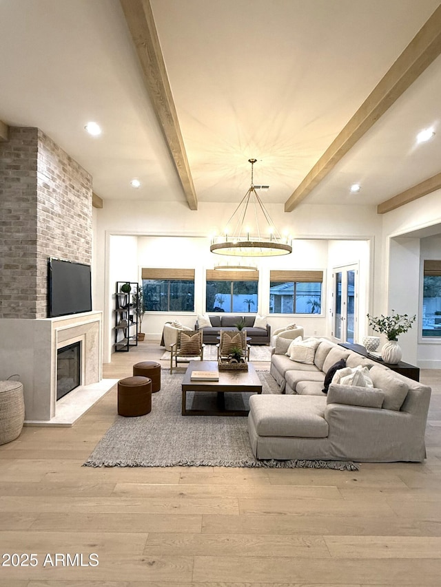 living room with beam ceiling, a fireplace, an inviting chandelier, and light hardwood / wood-style flooring