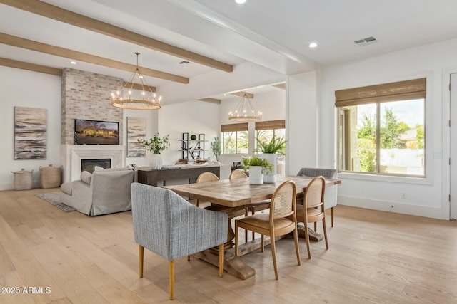 dining area featuring a large fireplace, beamed ceiling, a chandelier, and light hardwood / wood-style floors