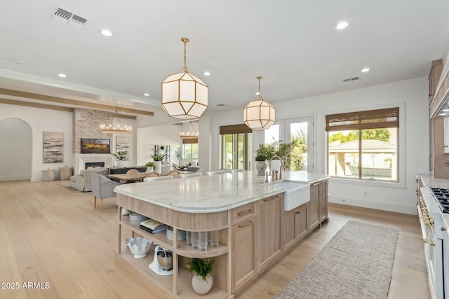 kitchen featuring decorative light fixtures, light brown cabinets, a fireplace, an island with sink, and sink