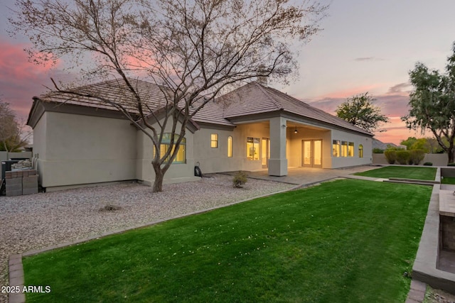 back house at dusk featuring a lawn and a patio