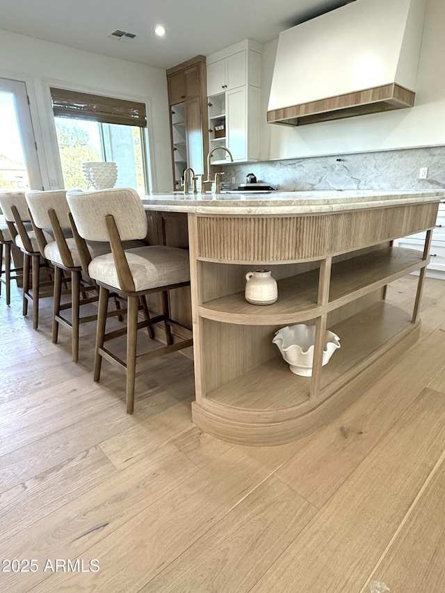 kitchen with premium range hood, white cabinets, sink, and light wood-type flooring