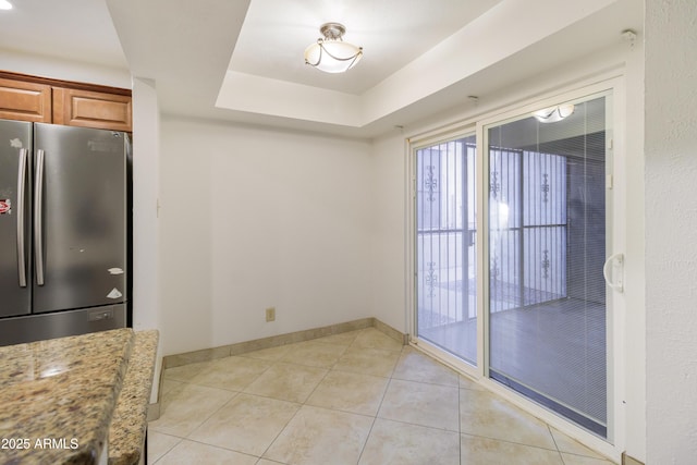 interior space featuring light stone counters, stainless steel fridge, a raised ceiling, and light tile patterned flooring