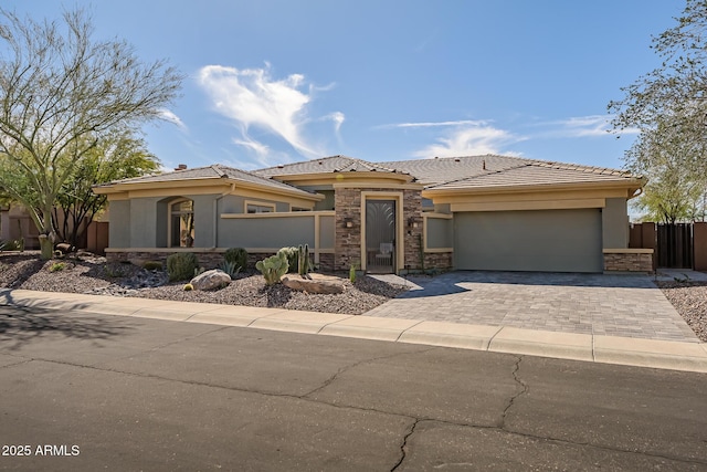 prairie-style house featuring an attached garage, stone siding, decorative driveway, and stucco siding