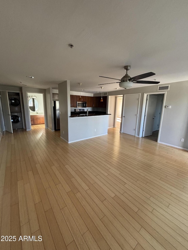 unfurnished living room with stacked washer / drying machine, baseboards, light wood-style floors, visible vents, and a ceiling fan