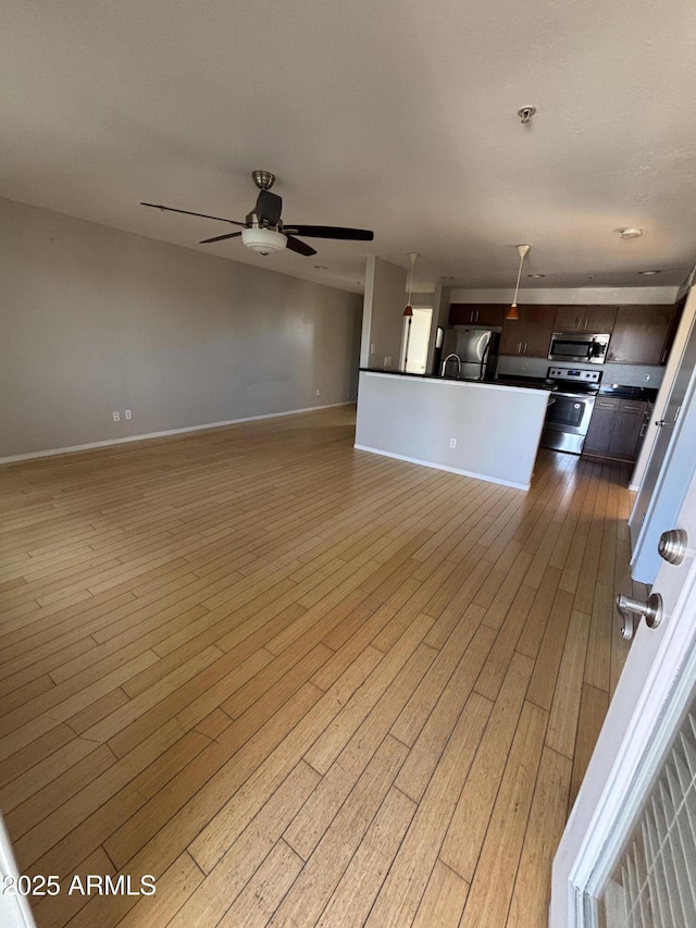 unfurnished living room featuring a ceiling fan, baseboards, and light wood-style floors