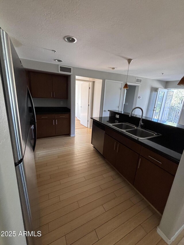 kitchen featuring visible vents, dark countertops, a sink, light wood-style floors, and freestanding refrigerator