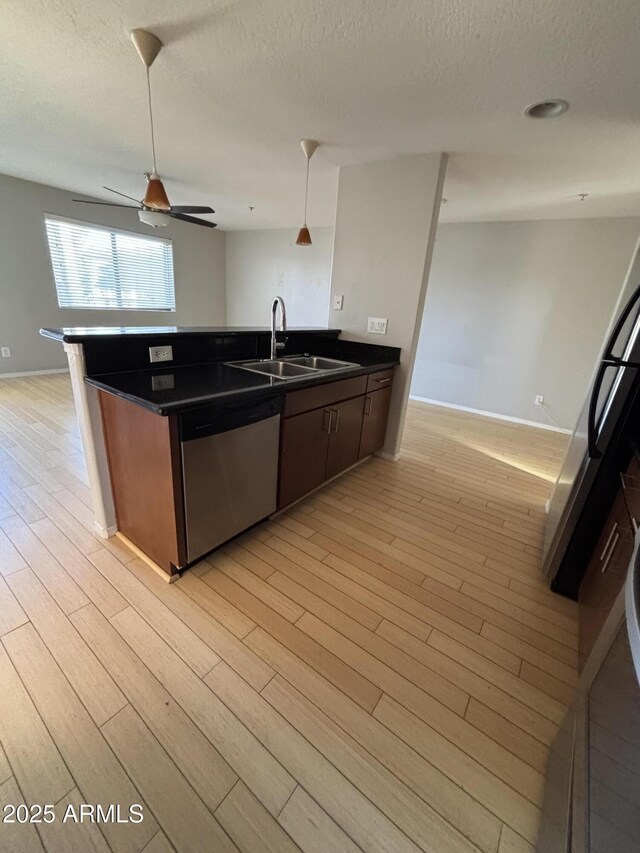 kitchen featuring a sink, stainless steel dishwasher, open floor plan, light wood-type flooring, and dark countertops