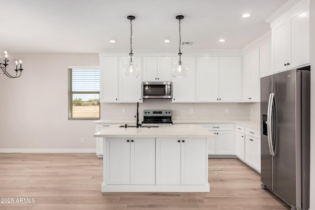 kitchen with appliances with stainless steel finishes, white cabinetry, hanging light fixtures, a center island with sink, and light wood-type flooring