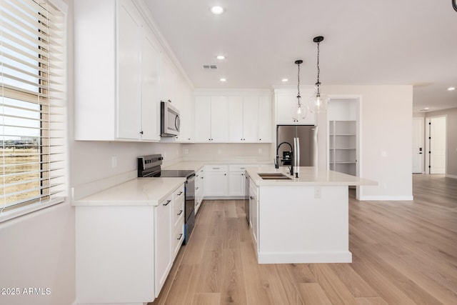 kitchen with sink, appliances with stainless steel finishes, white cabinets, a center island with sink, and decorative light fixtures