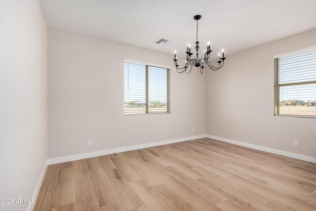 spare room with a wealth of natural light, a notable chandelier, and light wood-type flooring