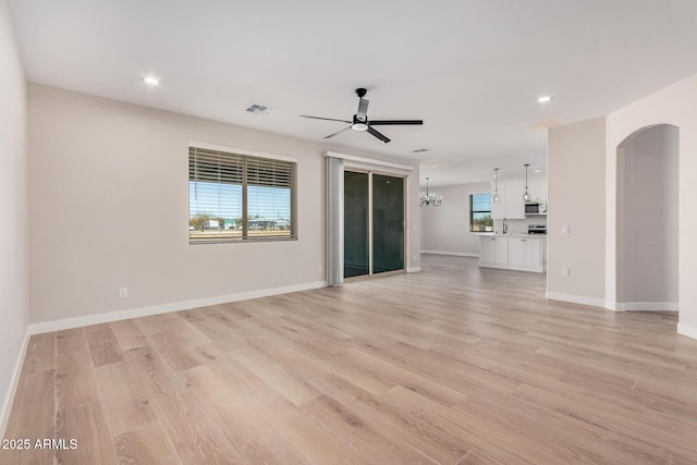 unfurnished living room with sink, ceiling fan with notable chandelier, and light wood-type flooring