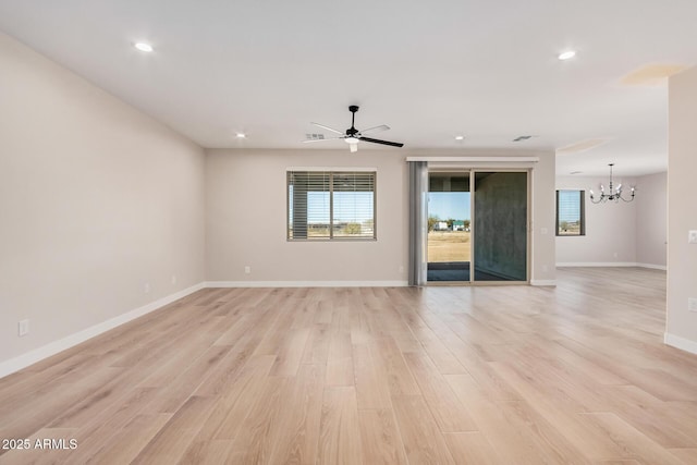 empty room featuring ceiling fan with notable chandelier, a healthy amount of sunlight, and light hardwood / wood-style floors