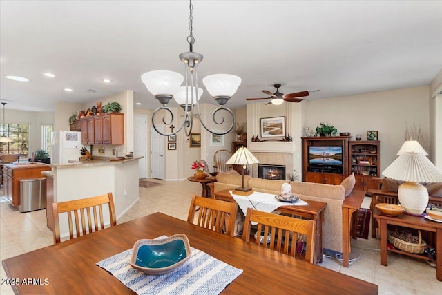 dining area featuring light tile patterned floors, ceiling fan with notable chandelier, a tile fireplace, and recessed lighting