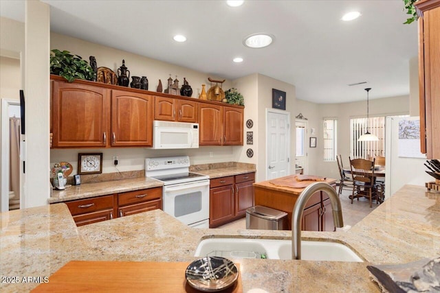 kitchen featuring white appliances, brown cabinetry, decorative light fixtures, light stone countertops, and a sink