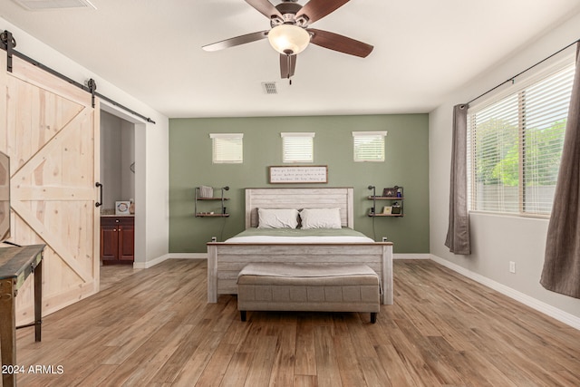 bedroom featuring a barn door, ceiling fan, light hardwood / wood-style flooring, and ensuite bath