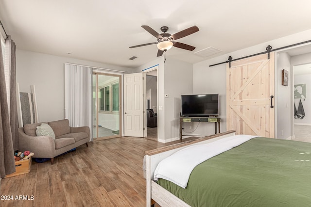 bedroom with a barn door, hardwood / wood-style floors, connected bathroom, and ceiling fan