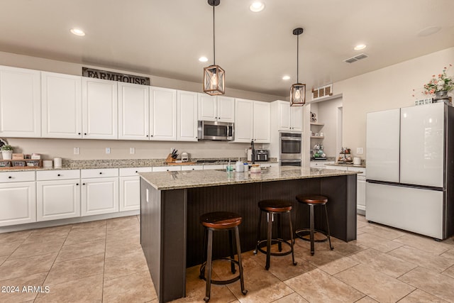 kitchen featuring light stone counters, decorative light fixtures, a center island with sink, white cabinetry, and appliances with stainless steel finishes