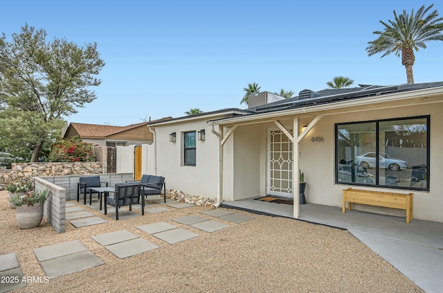 rear view of house with stucco siding, fence, solar panels, and a patio area