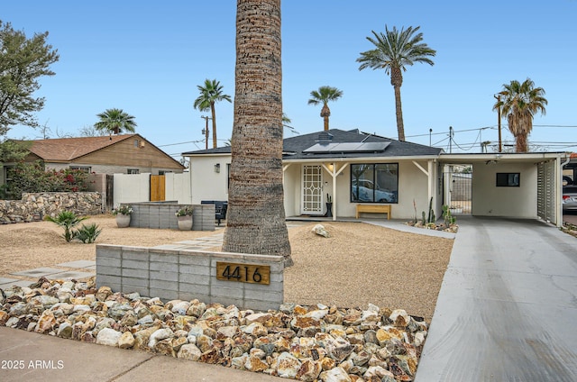 view of front facade featuring fence, roof mounted solar panels, stucco siding, an attached carport, and driveway