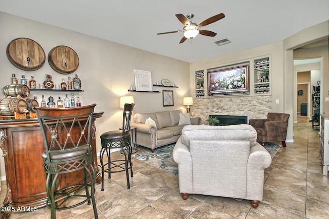 living room with a tile fireplace, bar, and ceiling fan