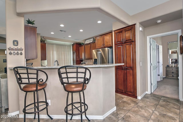 kitchen with light stone countertops, high quality fridge, a kitchen breakfast bar, and kitchen peninsula