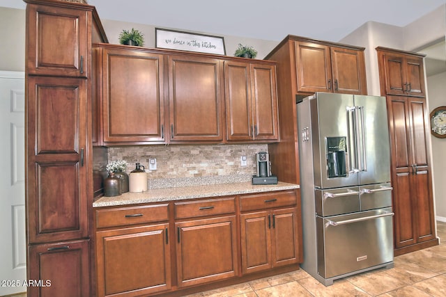 kitchen with light tile patterned flooring, high end fridge, backsplash, and light stone counters