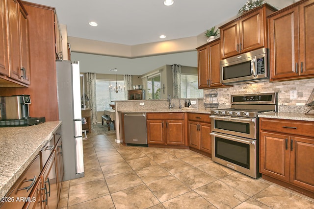 kitchen with hanging light fixtures, appliances with stainless steel finishes, backsplash, and light stone counters