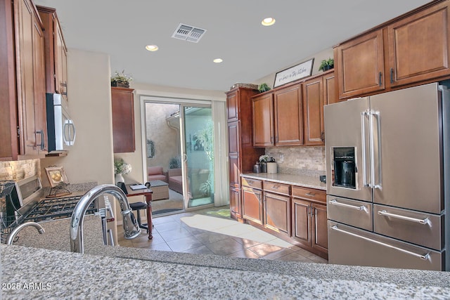 kitchen featuring light tile patterned flooring, appliances with stainless steel finishes, light stone countertops, and decorative backsplash