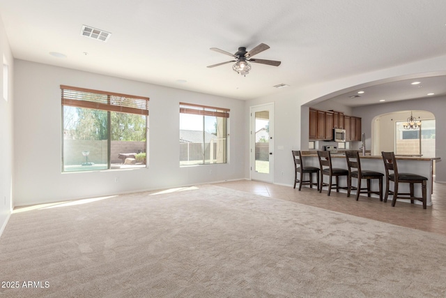 living area featuring light carpet, light tile patterned floors, ceiling fan with notable chandelier, visible vents, and arched walkways