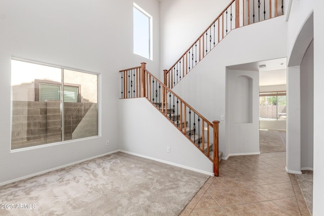 interior space featuring stairs, baseboards, tile patterned floors, a towering ceiling, and arched walkways