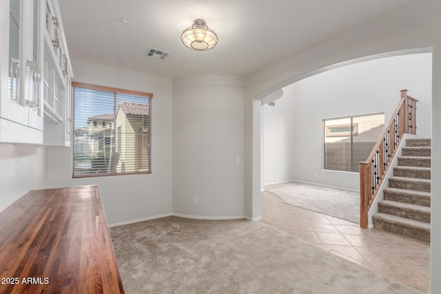 tiled spare room featuring visible vents, carpet, baseboards, stairs, and arched walkways