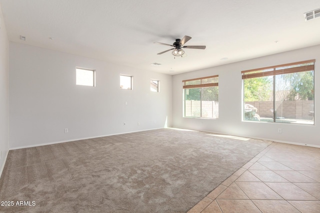 spare room with light colored carpet, baseboards, light tile patterned flooring, ceiling fan, and visible vents