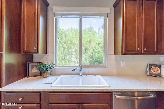 kitchen with stainless steel dishwasher, tasteful backsplash, a sink, and brown cabinetry