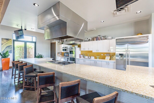 kitchen with white cabinetry, stainless steel appliances, a kitchen breakfast bar, island range hood, and light stone countertops